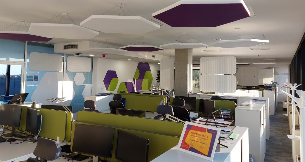 Interno di un ufficio dove è stato fatto trattamento acustico con pannelli fonoassorbenti verdi e viola sia in parete che nel soffitto e fra le varie postazioni di lavoro